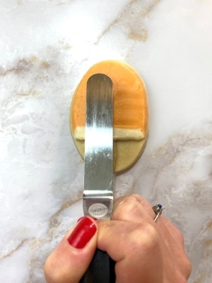 orange flavored buttercream on creamsicle cookie, holding angled flat spatula up to cookie